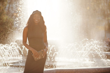 Stylish african american girl in gray tunic, crossbody bag and cap posed at sunny autumn day against fountains. Africa model woman. - obrazy, fototapety, plakaty