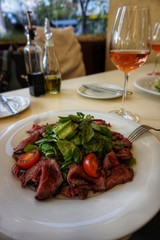 Delicious lunch at the restaurant: slices of meat and salad on a white porcelain plate.