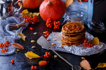 Autumn concept. Pumpkin pancakes with caramel topping, with pumpkins, leaves on a dark background.
