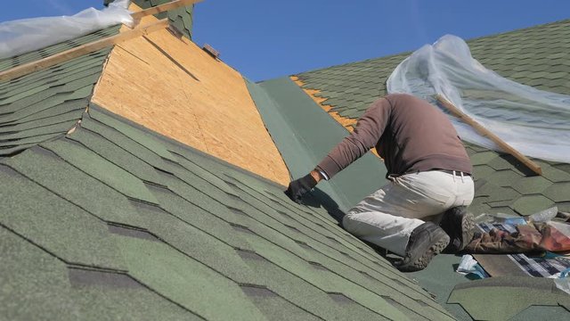 soft roof of shingles. Repair of the roof of a residential house. installation of soft tiles. partial replacement of the damaged roof. Dot repair. carpenter throws a hammer up and catches it. Worker