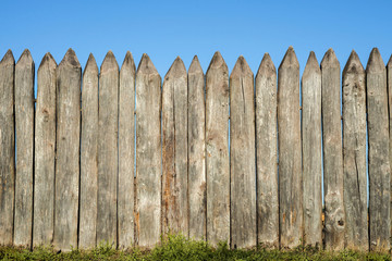 Fence made of sharp wooden stakes against the blue sky. Wooden fence vertical logs pointed against...