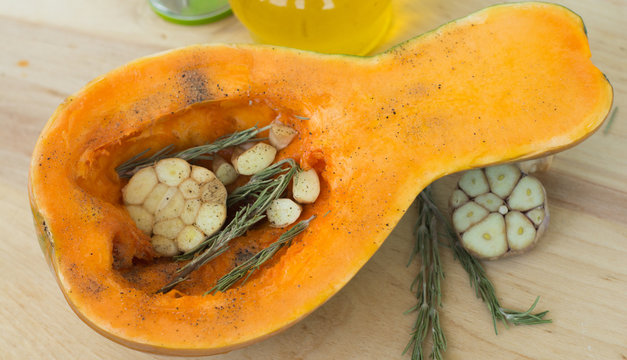 raw pumpkin, rosemary and garlic on wooden background