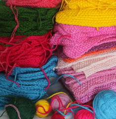 Piles of knitted colorful patches with threads and balls of yarn. 