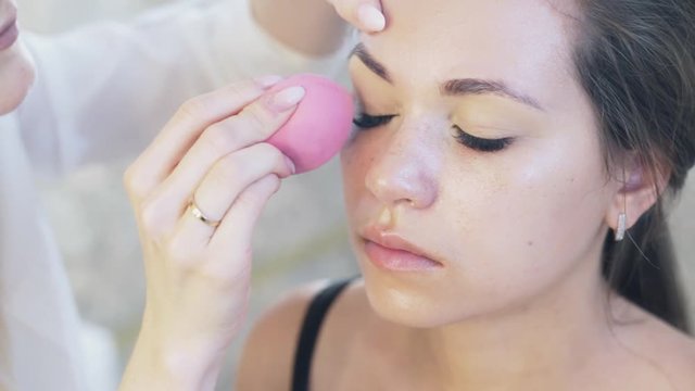 Close-up cropped frame of young women came to the makeup. The make-up artist interprets concealer on the upper eyelid to the client, inflates it with the help of small paralon balls. Slow-motion.