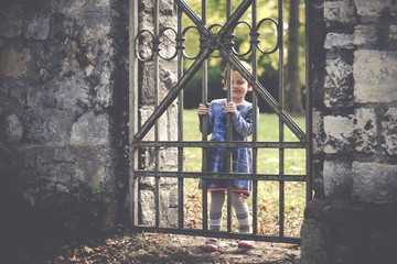 Portrait of a small four year old girl at a old iron gate in a park in autumn.
