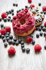 Baked donuts with dried raspberry and a chocolate on the wooden table. The doughnut with many fresh blueberries and raspberry. Rural bakery concept.