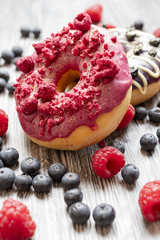 Baked donuts with dried raspberry and a chocolate on the wooden table. The doughnut with many fresh blueberries and raspberry. Rural bakery concept.