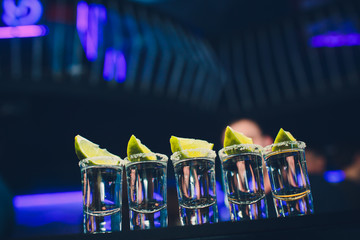 Silver tequila shots with ice and lime on black table background.