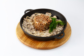 beef stroganoff with buckwheat and greens in a cast iron pan, isolated on white background