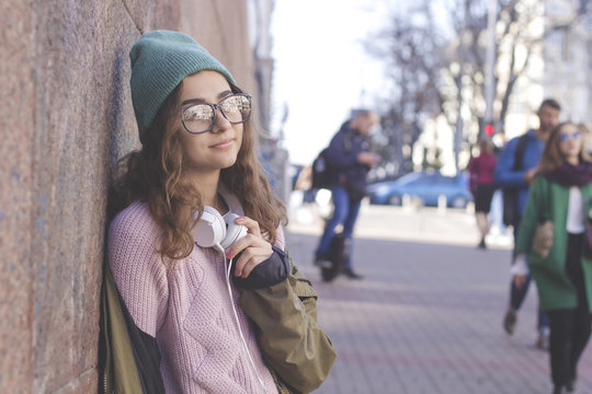 Cute teen girl in a hat and headphones on a city street. Young stylish woman outdoor.