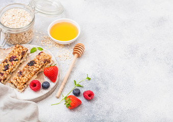 Organic cereal granola bar with berries on round vintage board with honey spoon and jar of oats on marble background. Strawberry, raspberry and blueberry with mint leaf and bowl of honey
