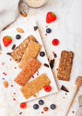 Organic cereal granola bar with berries on marble board with honey spoon and jar of oats and linen towel on marble background.