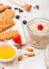 Organic cereal granola bar with berries on marble board with honey spoon and jar of oats and coconut on marble background. Top view