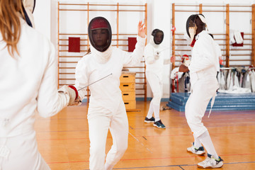 Two female fencers  exercising movements in duel at fencing room