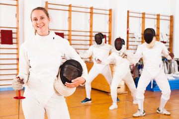 Smiling young female in uniform standing at fencing room