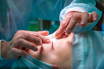 Surgeon and his assistant performing cosmetic surgery on nose in hospital operating room. Nose...