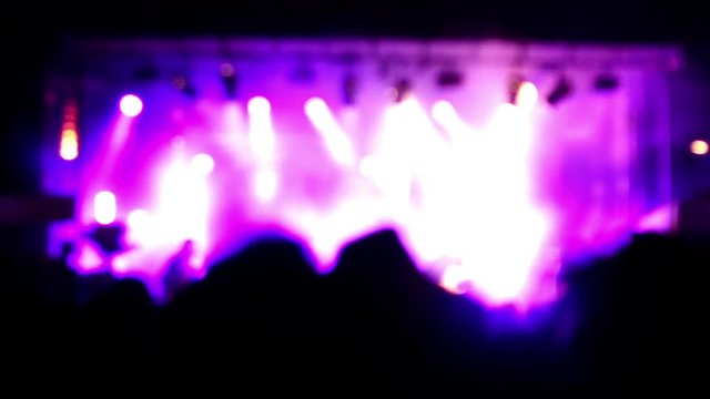 Blurred scene of a rock concert with musicians on stage and the crowd in the shadow. Purple lighting effects. Abstract picture for background.