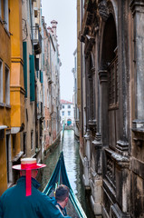 Venetian gondolier punting gondola through green little canal waters of Venice Italy