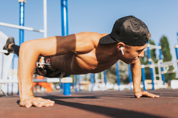 Closeup horizontal image of young athletic muscular man doing push-ups on sports ground outdoor. Caucasian shirtless fitness male doing outdoor workout exercises outside. People and sport concept