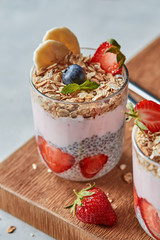 Glass of fruit smoothie and fresh berries with oat homemade granola, chia seeds on a wooden board on a gray.