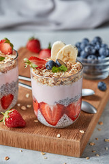 Dietary natural breakfast with fresh organic ingredients - berries, granola, banana in a glass on a wooden table. Healthy vegetarian eating.