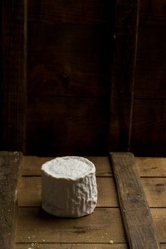 Whole head of brie cheese on wooden board on dark background