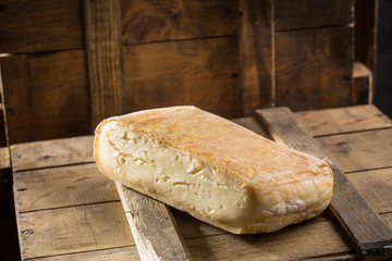 Piece of taleggio cheese on wooden board on dark background