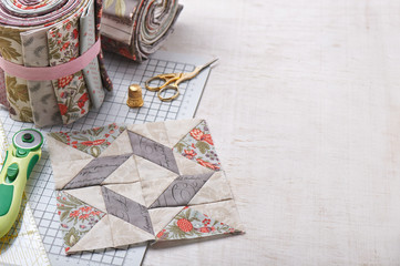 Patchwork block on craft mat, rolls of fabric, sewing accessories on white wooden surface - obrazy, fototapety, plakaty