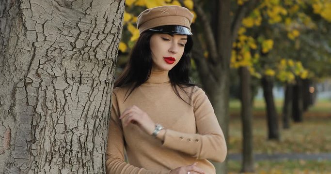 Glamourous woman waiting her friend leaning on tree, autumn day