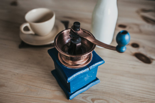 Vintage manual coffee grinder of blue color from wood and copper, milk and a cup - making coffee