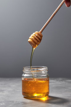Sweet flower natural honey dripping to a glass jat with yellow transparent dessert on a gray background. Rosh hashanah jewish New Year holiday