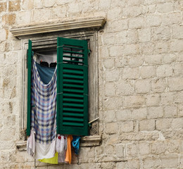 Fototapeta na wymiar Washing hanging from window, half hidden by green shutters. Stonework of building background. Budva, Montenegro.