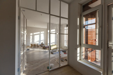 Interior empty office light room with white wallpaper without furniture in a new building renovation or under construction.Glass doors and Windows.