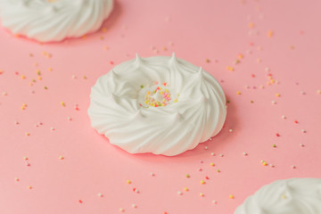 homemade white air meringues and confectionery decorations on pink background