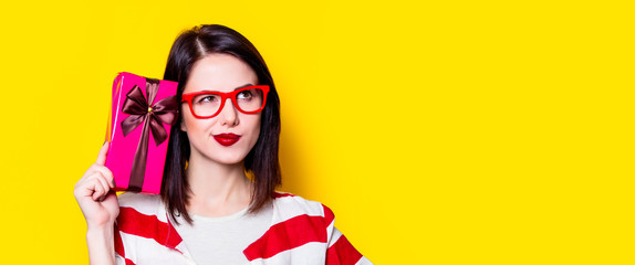 Portrait of a young woman in glasses with gift box on yellow background