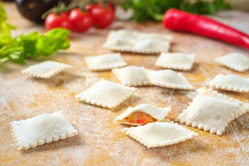 raw colored ravioli ravioli in flour with vegetables and tomatoes on wooden background. Process of making italian pasta