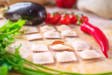 raw colored ravioli with flour and tomatoes on wooden background. Process of making italian pasta