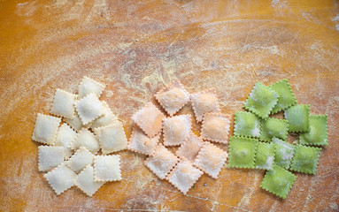 Multi-colored uncooked ravioli on a cutting board, sprinkled with flour, handmade, on a wooden table. Top view, copy space