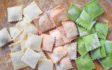 Multi-colored uncooked ravioli on a cutting board, sprinkled with flour, handmade, on a wooden table. Top view, closeup