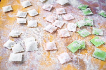Multi-colored uncooked ravioli on a cutting board, sprinkled with flour, handmade, on a wooden table. cooking process