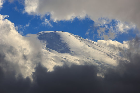 The western peak of Mount Elbrus, the slope with snow is visible through the clouds. Mountain range in the North Caucasus in Russia.
