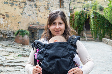 Beautiful young mother with baby child in carrier in the old town. Active travel family vacation