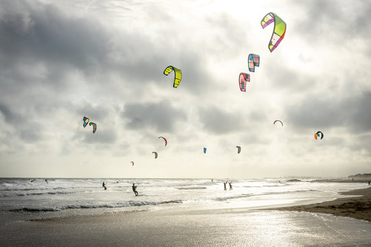 un ciel gris au dessus d'une plage en contre jour avec des voiles  de kitesurf 