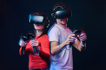Young couple playing video games wearing virtual reality glasses with controllers.