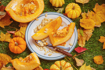 Orange pumpkin on a plate and leaves on a green lawn