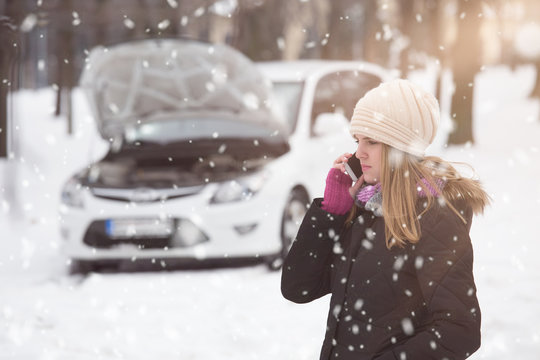 Young Woman Using Smartphone To Call Road Assistance. Winter And Vehicle Concept.