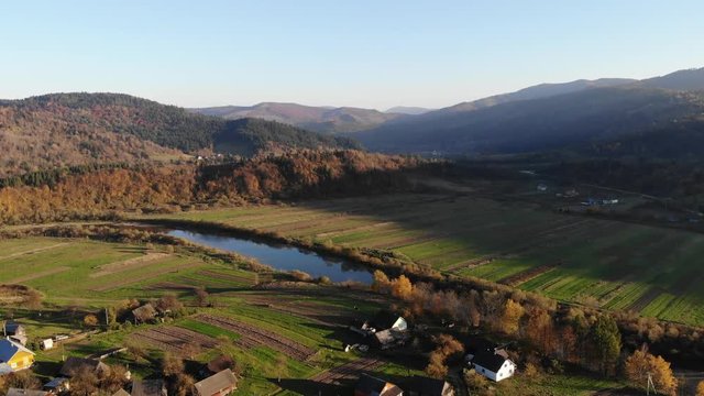 Smooth flight over the old village and river in the Carpathian valley, Ukraine. Autumn time, aerial view