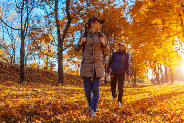 Tourists with backpacks walking in autumn forest. Mother and her adult daughter travelling together
