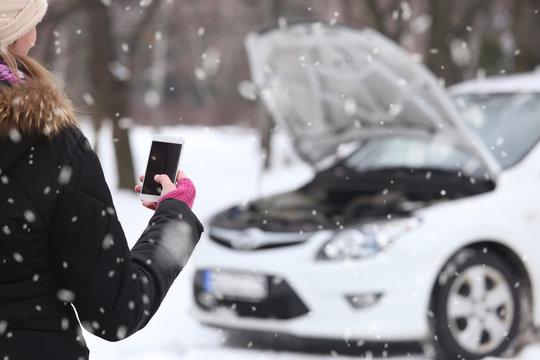 Close up of woman hand in woolen gloves holding blank screen smart phone. Broken car in background.
