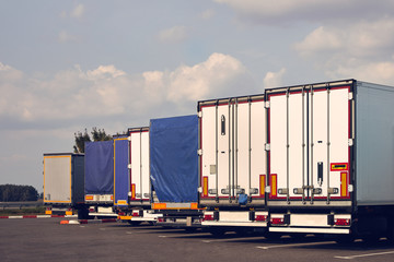 Modern trucks of various models are in a row on truck stop. Back view.